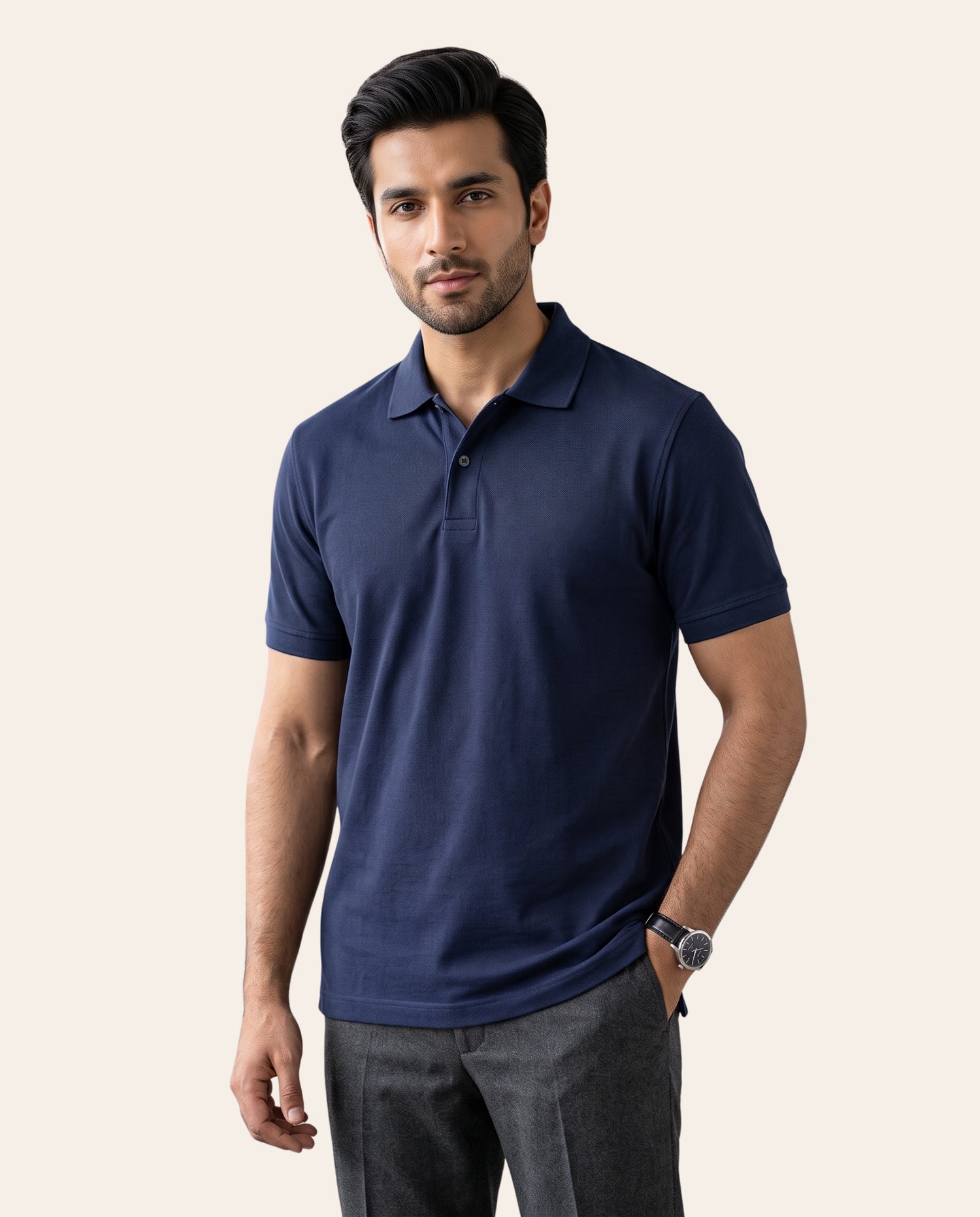 A man wearing a navy blue short-sleeve polo shirt and dark gray trousers, standing against a solid light beige background.