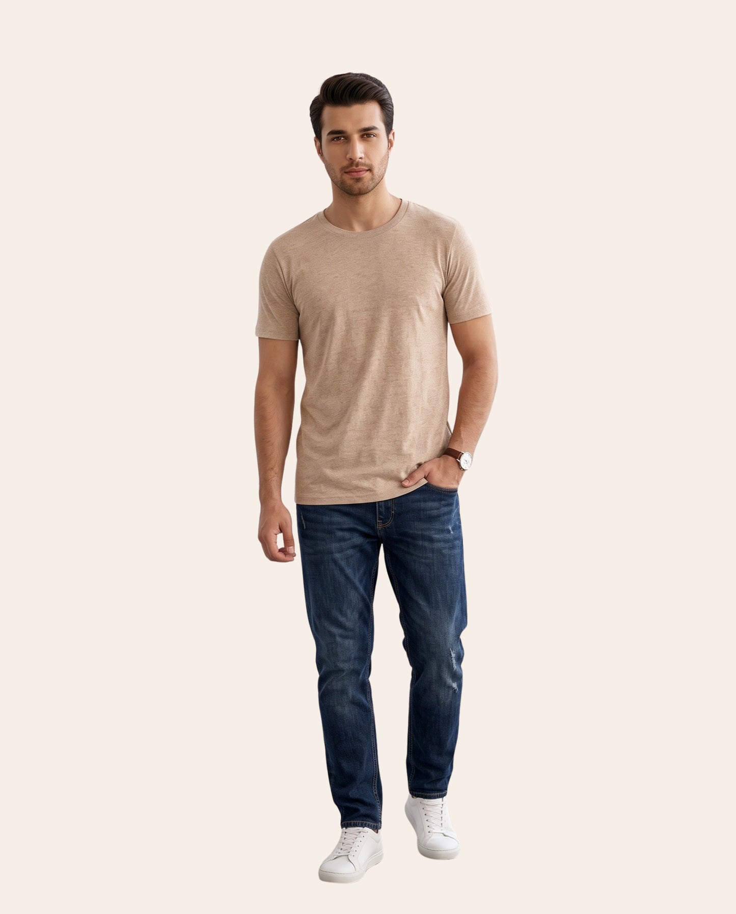 A man modeling a light beige short-sleeve crewneck t-shirt, paired with dark blue jeans and white sneakers, against a solid pale beige background.